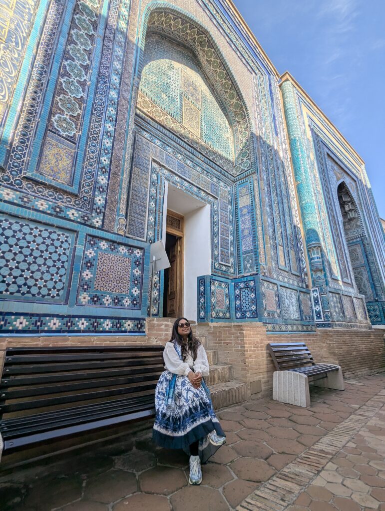 Traveller sitting at Shah-i-Zinda necropolis Samarkand Uzbekistan surrounded by intricate blue tile mosaic architecture